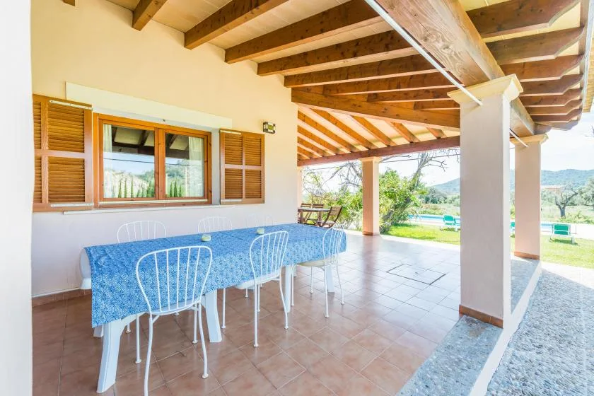 Comedor exterior cubierto con una mesa junto a ventanas con contraventanas.