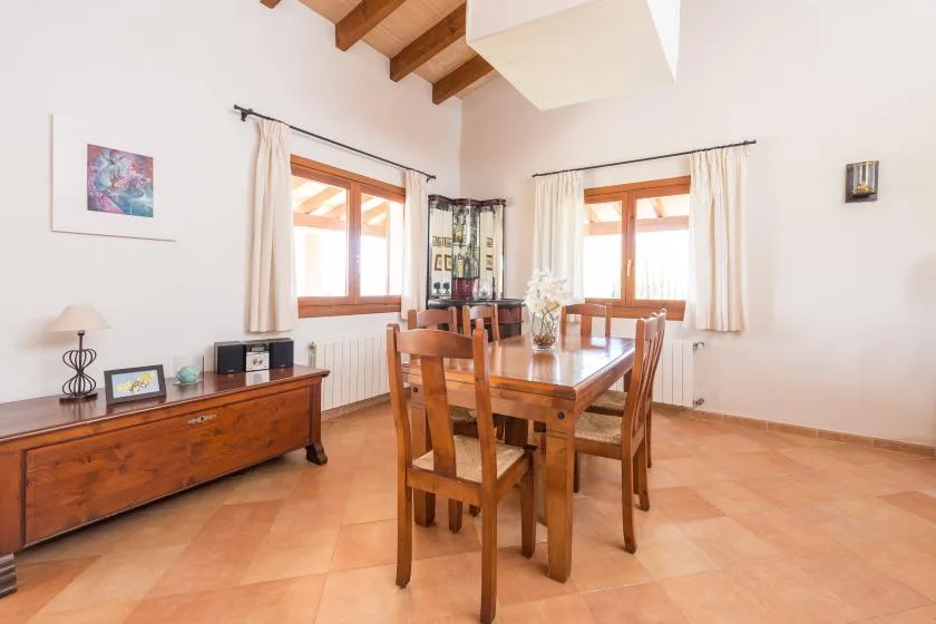 Un comedor con una mesa de madera y sillas junto a dos ventanas luminosas.