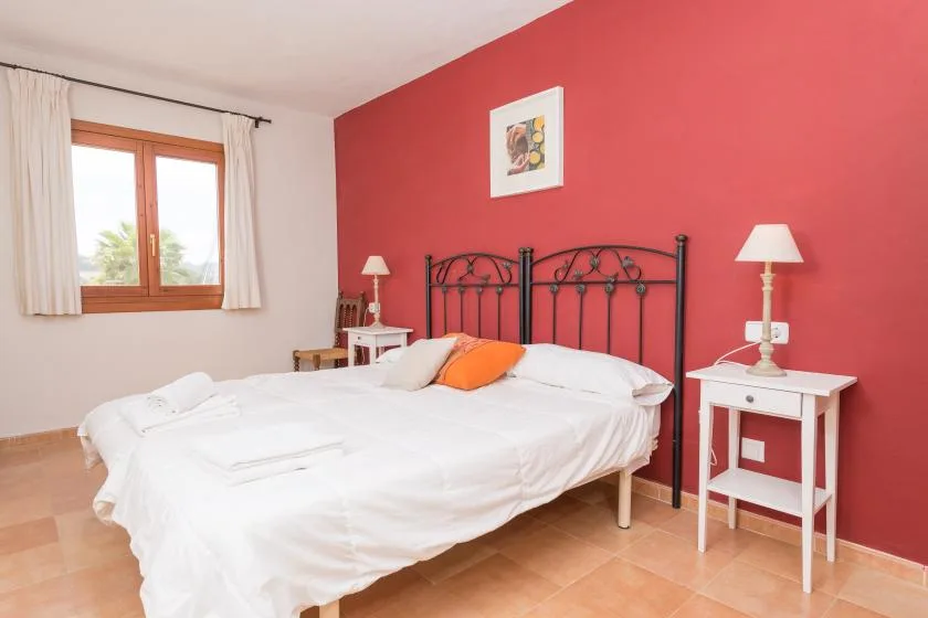 Un dormitorio con una cama doble, ropa de cama blanca y una pared roja.