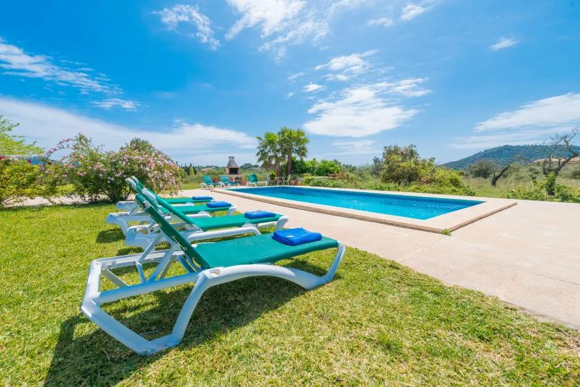 Una piscina junto a un césped con tumbonas.