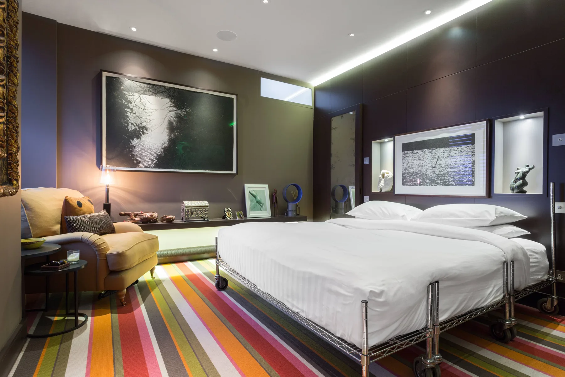 A bedroom with a large bed, colorful striped rug, and seating area.