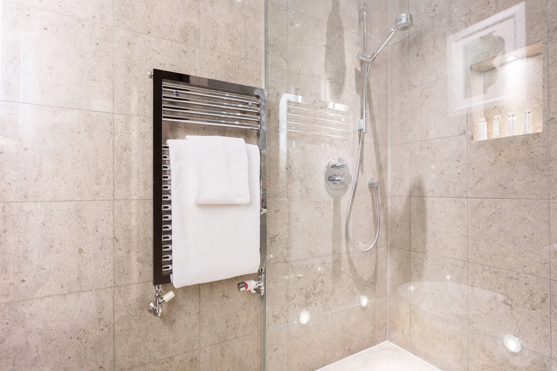 A tiled bathroom shower with a wall-mounted towel warmer and folded towels.