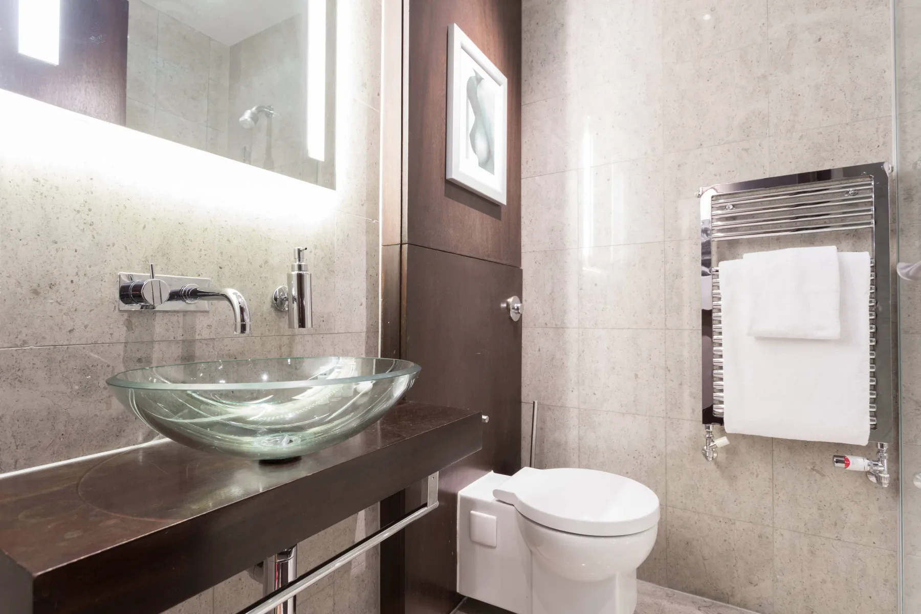 A modern bathroom with a glass vessel sink, toilet, and towel warmer.