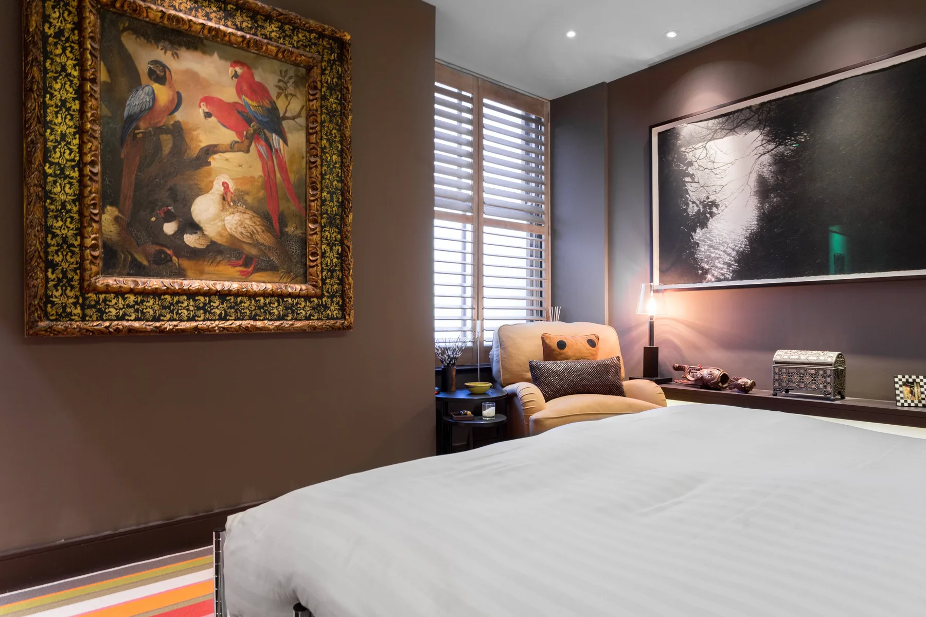 A bedroom with a bed, a chair, and framed artwork on the walls.