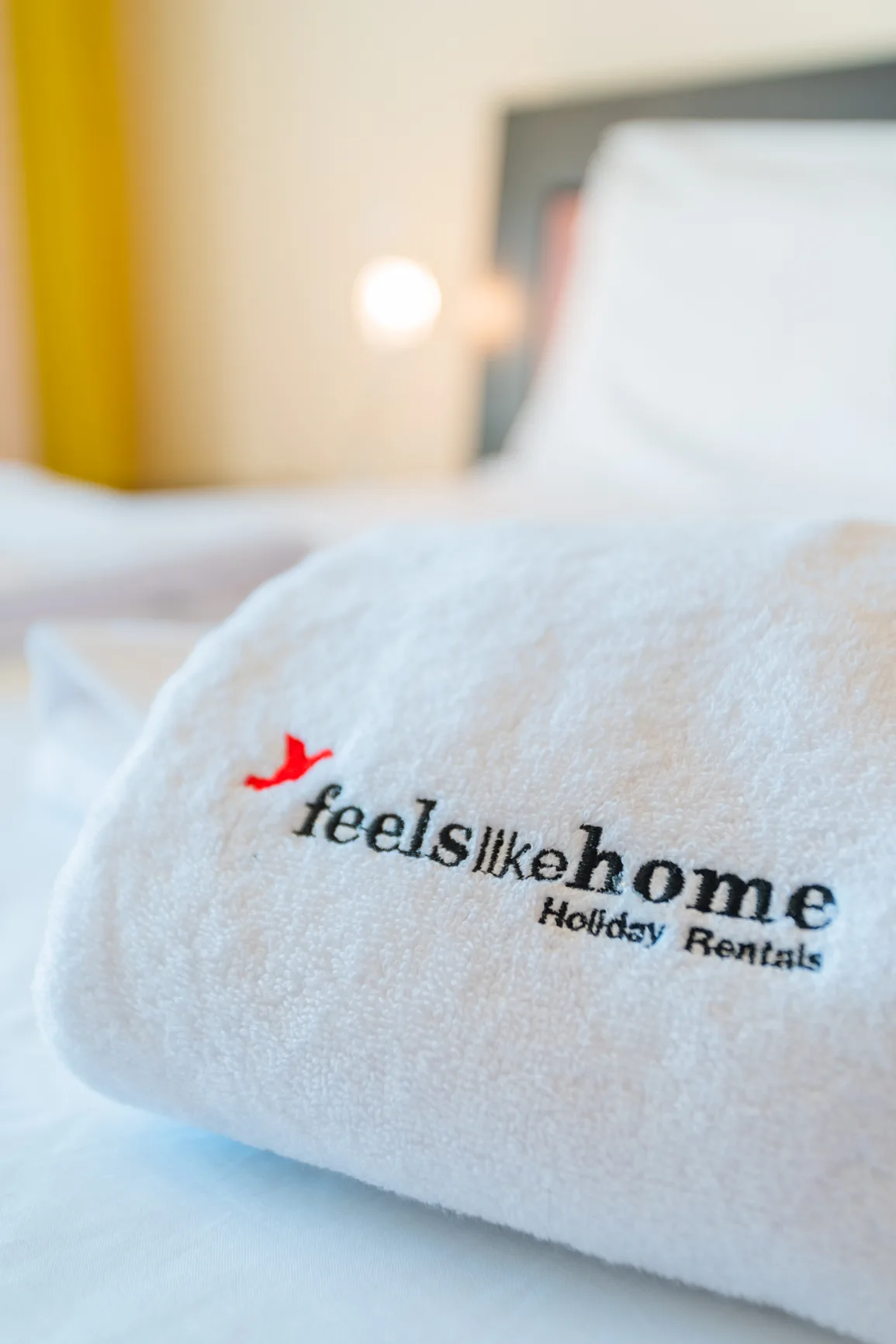 A bedroom with a white towel embroidered with a rental logo on the bed.