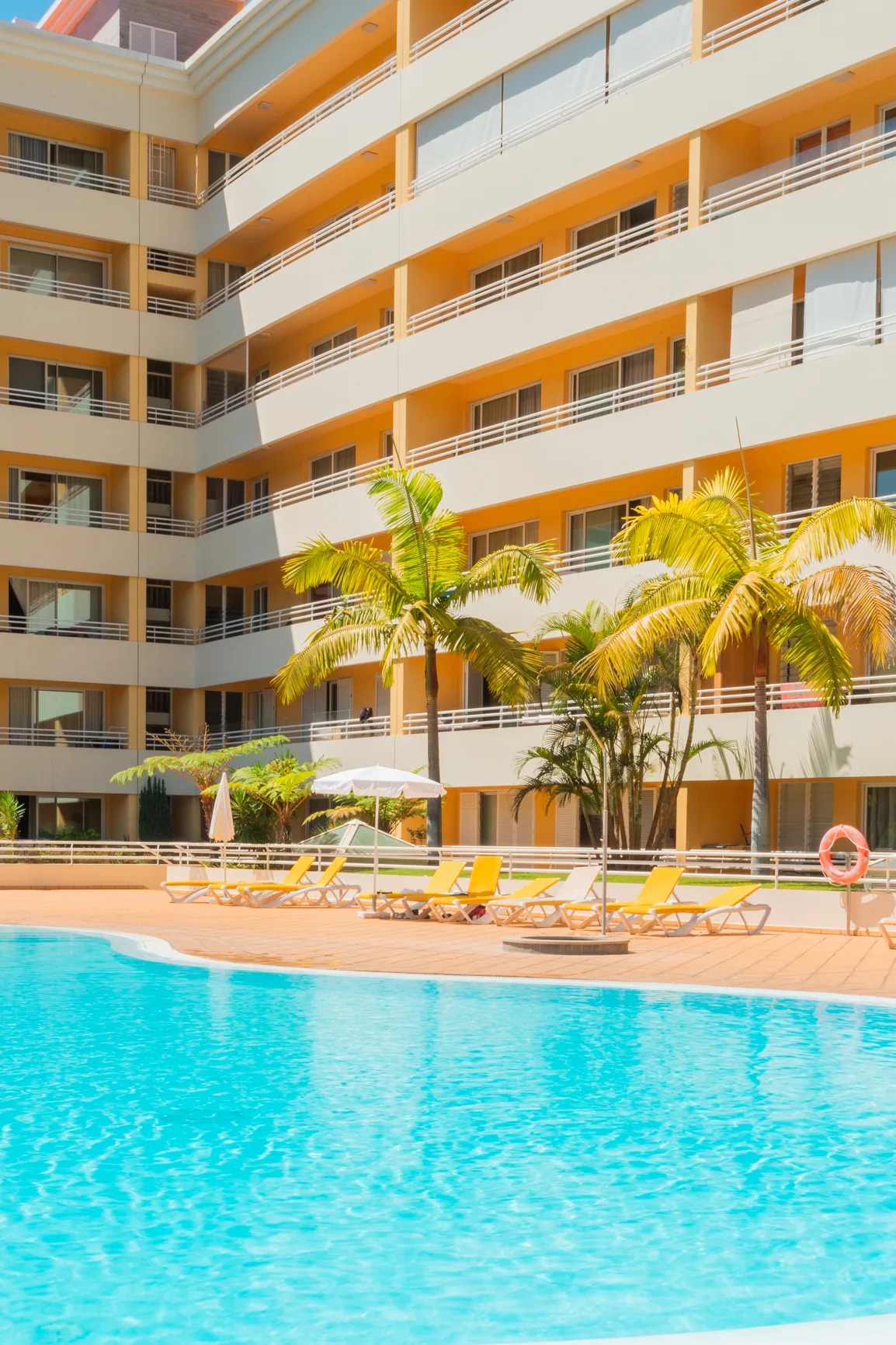 A swimming pool with lounge seating sits in front of a multi-story building.
