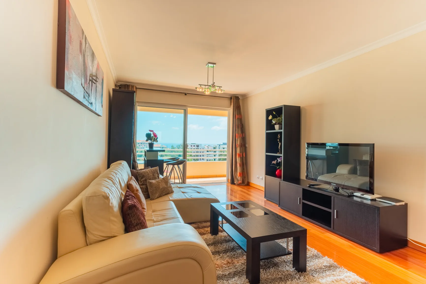 A living room with a sofa, coffee table, and television beside a balcony.