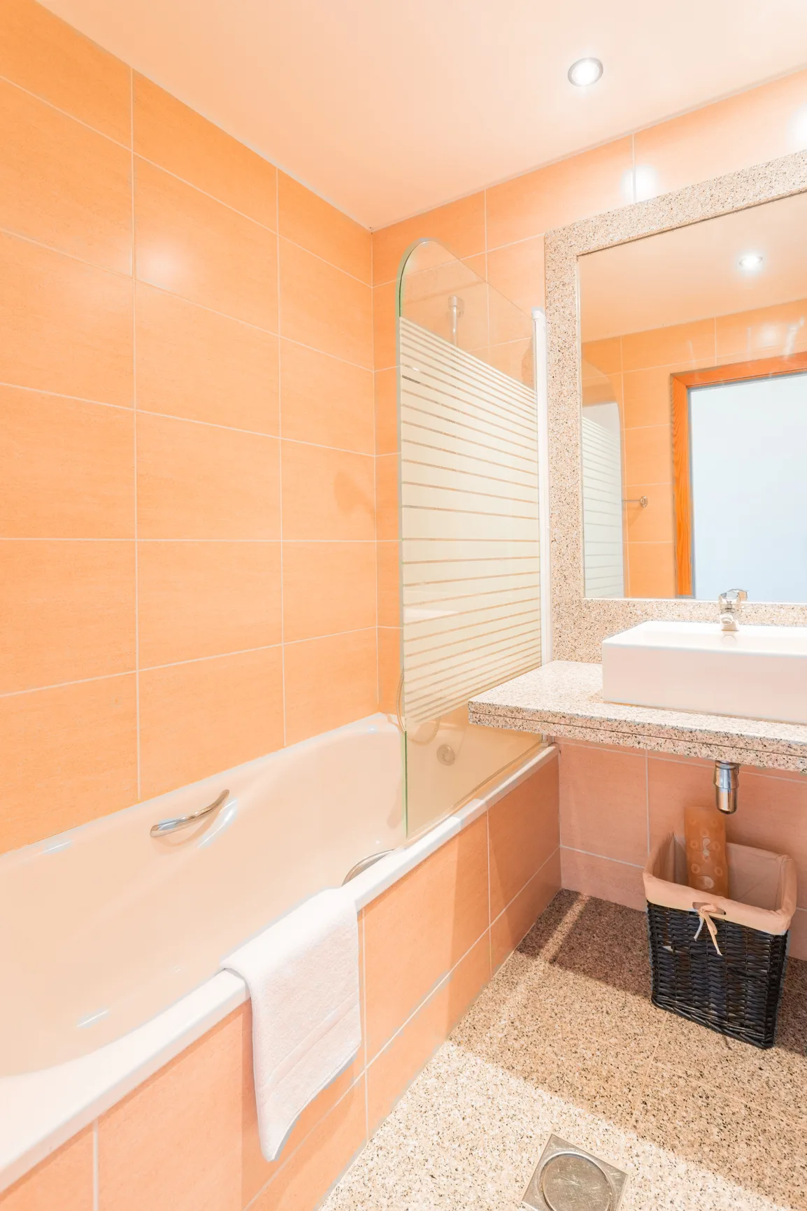 A bathroom with a bathtub, glass screen, and sink.