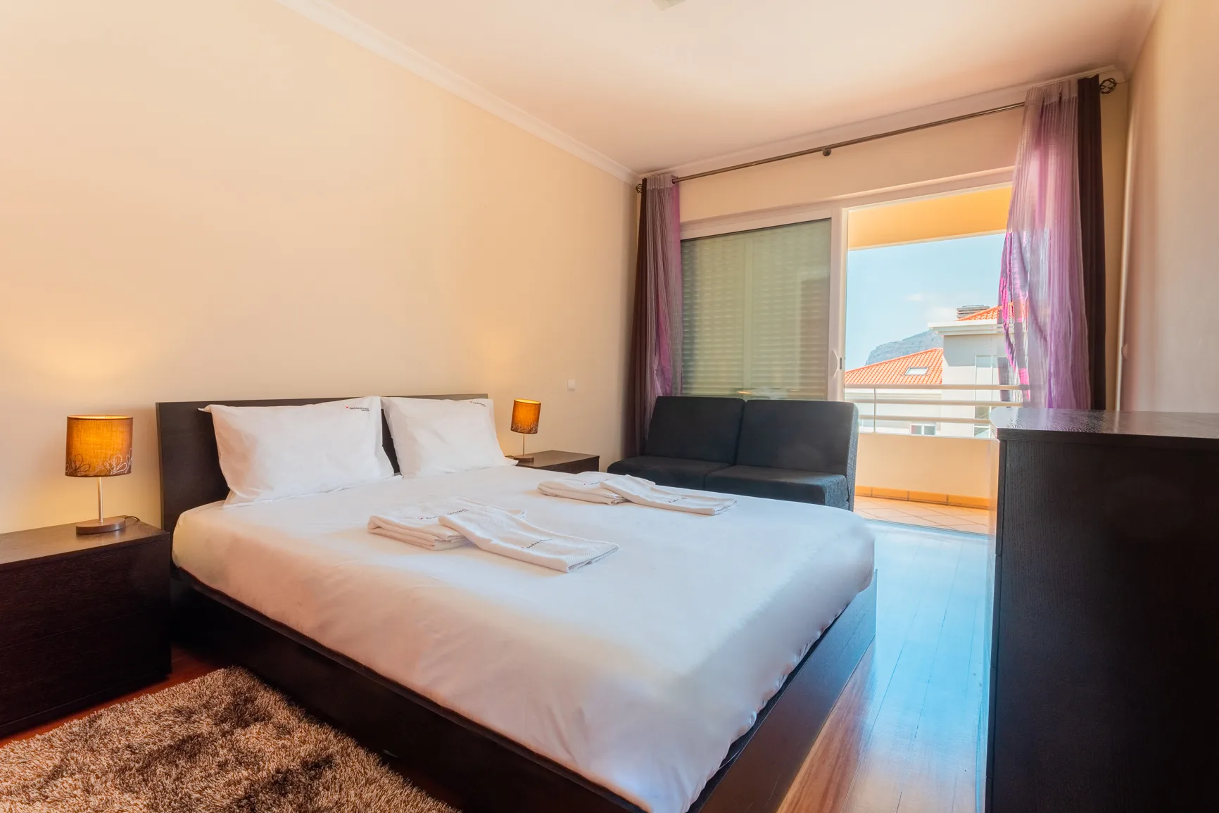 A bedroom with a large bed and a sliding glass door to a balcony.