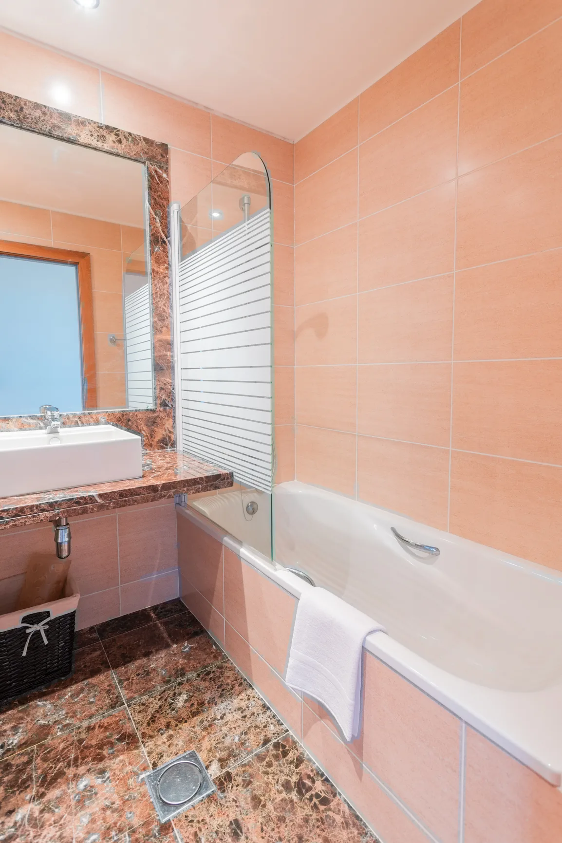 A tiled bathroom with a bathtub, glass shower screen, and sink.