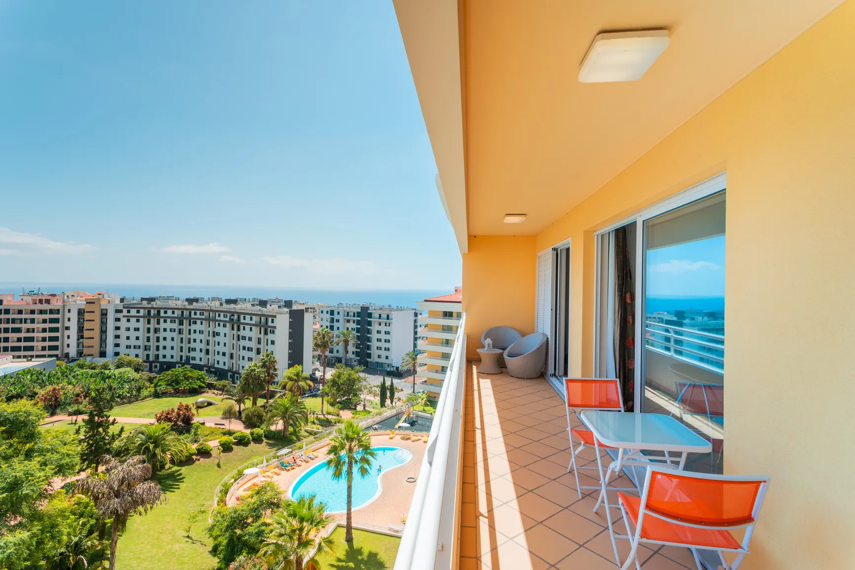 A furnished balcony overlooks a swimming pool and landscaped grounds.