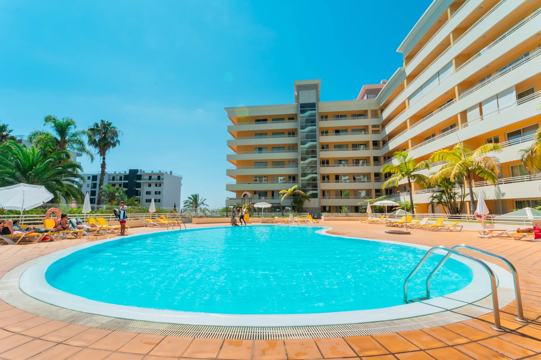 An outdoor swimming pool sits beside a large apartment building.
