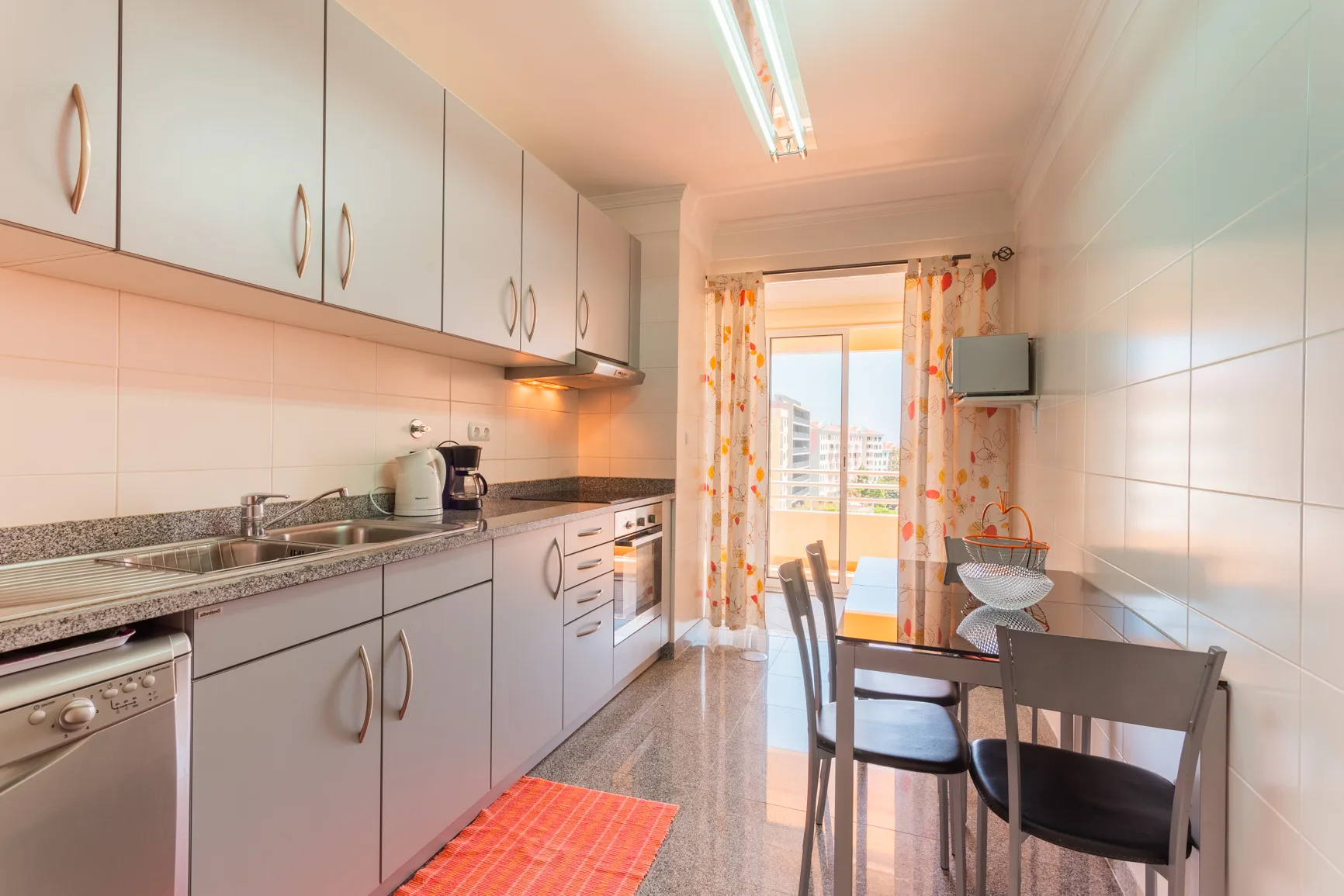 A tiled kitchen with cabinets, a counter, and a dining table by the window.