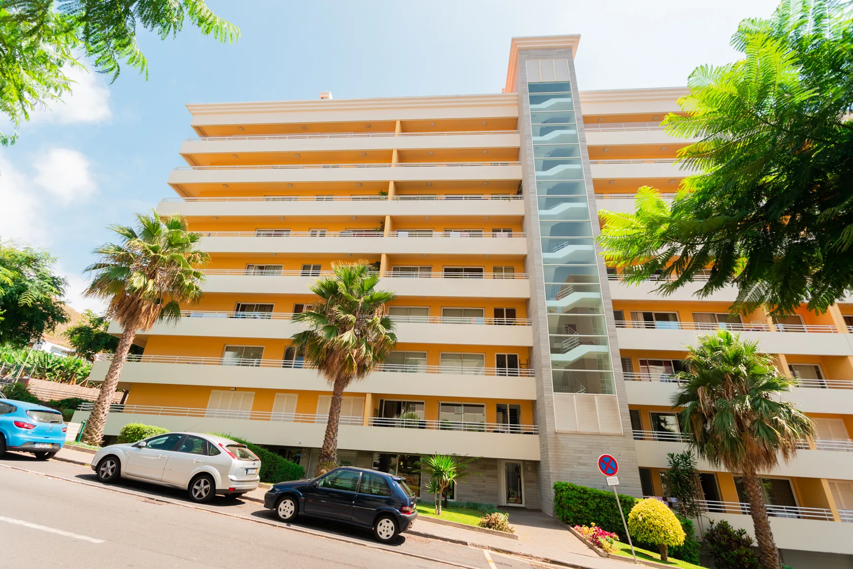 An apartment building with balconies and palm trees along the street.