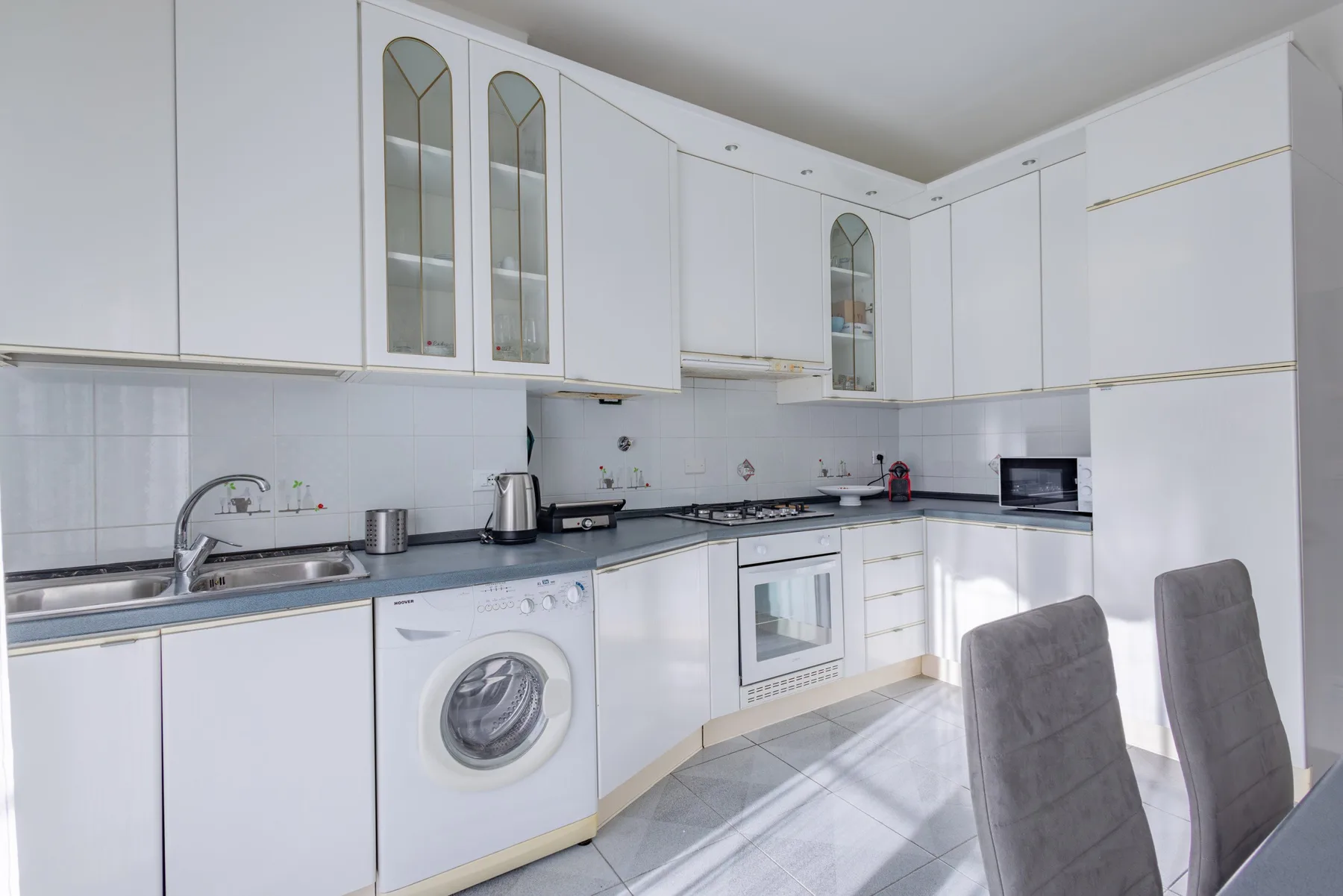 A bright kitchen with white cabinets, a washing machine, and a built-in oven.