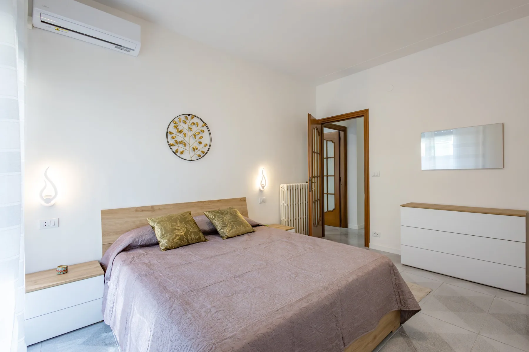 A bedroom with a neatly made bed, bedside tables, and an open doorway.