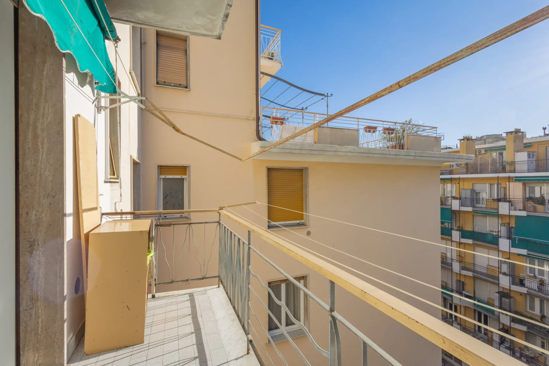 A narrow balcony with a metal railing overlooks neighboring apartment buildings.
