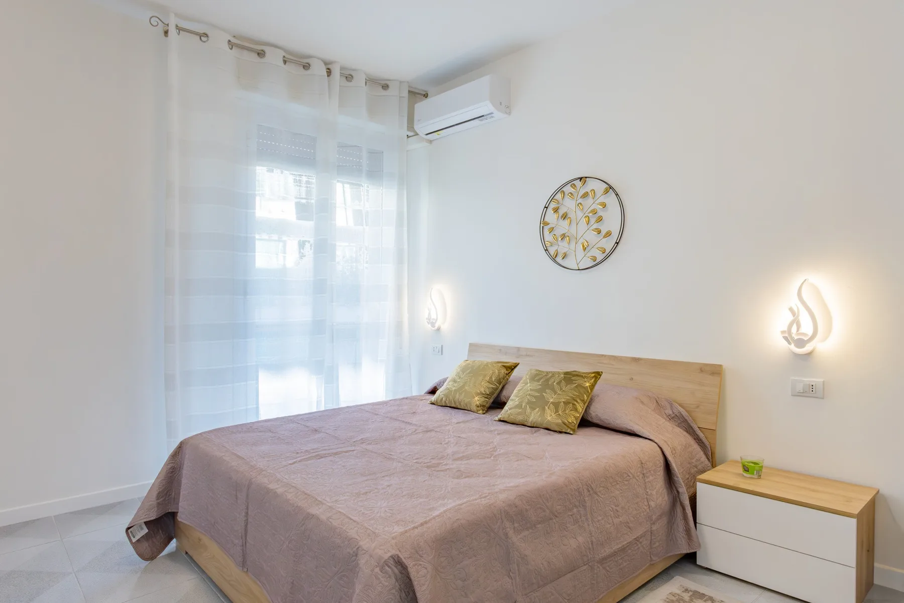 A bedroom with a double bed, bedside table, and sheer curtains.
