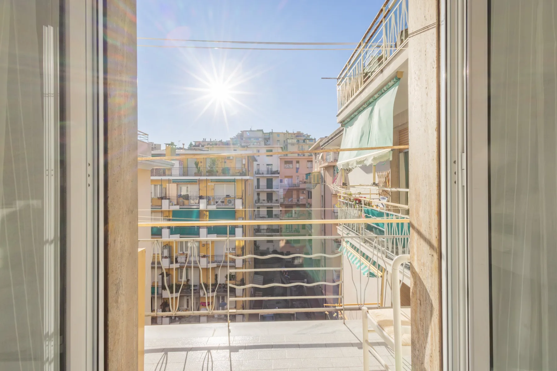 A sunny balcony overlooks neighboring apartment buildings.
