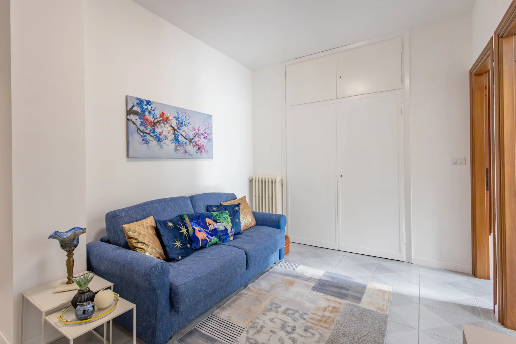 A living room with blue seating, colorful wall art, and a patterned rug.