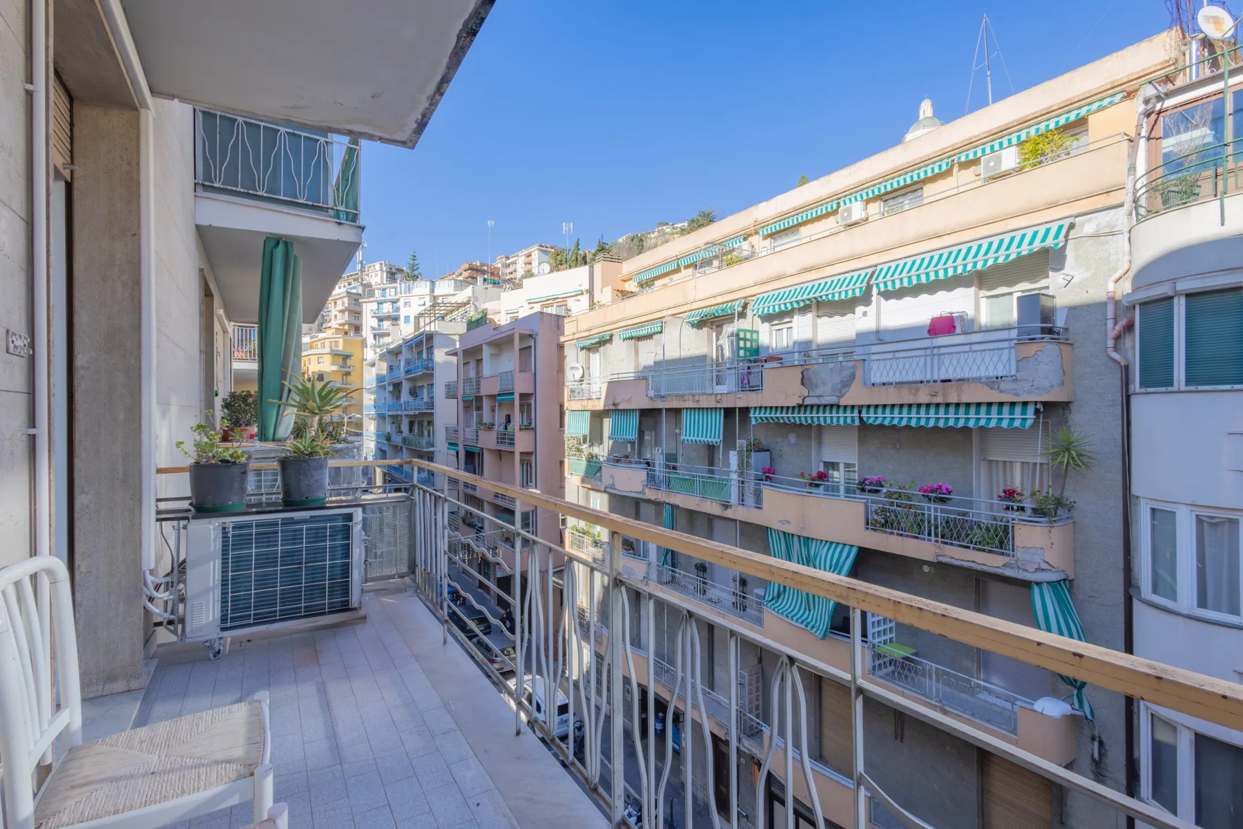A balcony overlooks neighboring apartment buildings beneath a clear blue sky.