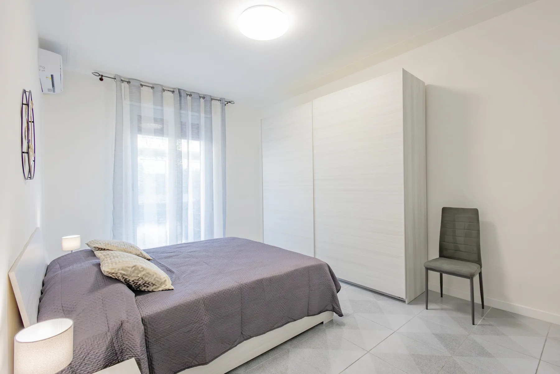 A bedroom with a bed, a curtained window, and a chair.