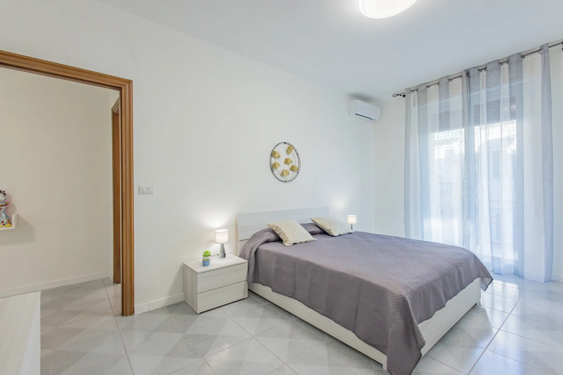 A bedroom with a double bed beside a large curtained window.