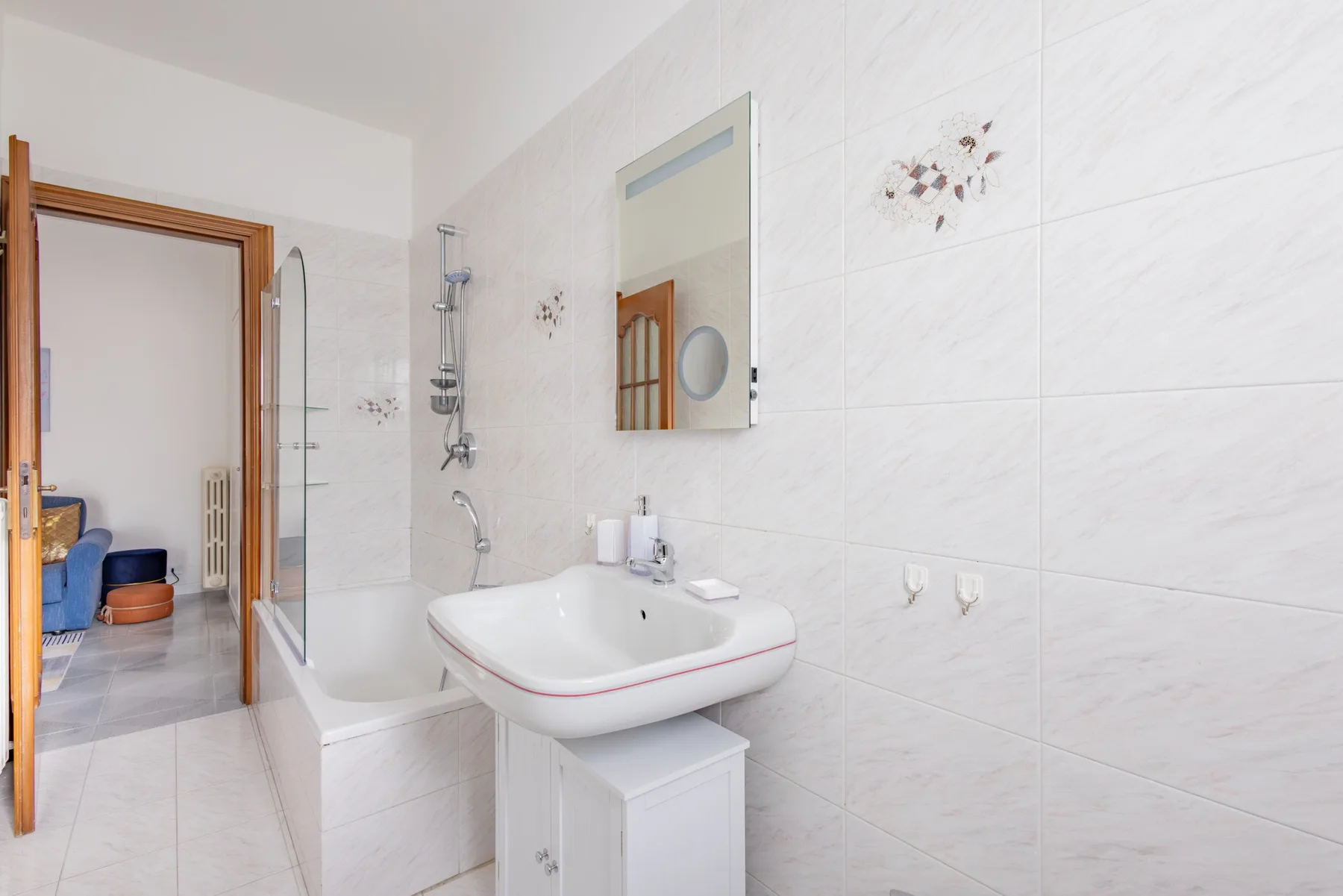 A tiled bathroom with a bathtub, shower fixtures, and a wall-mounted sink.