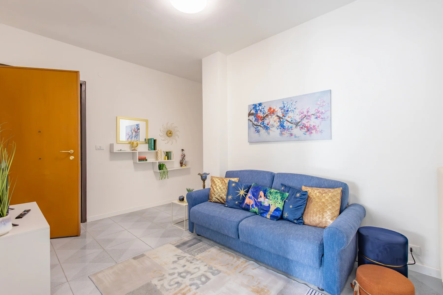 A living room with blue seating and colorful artwork on the wall.