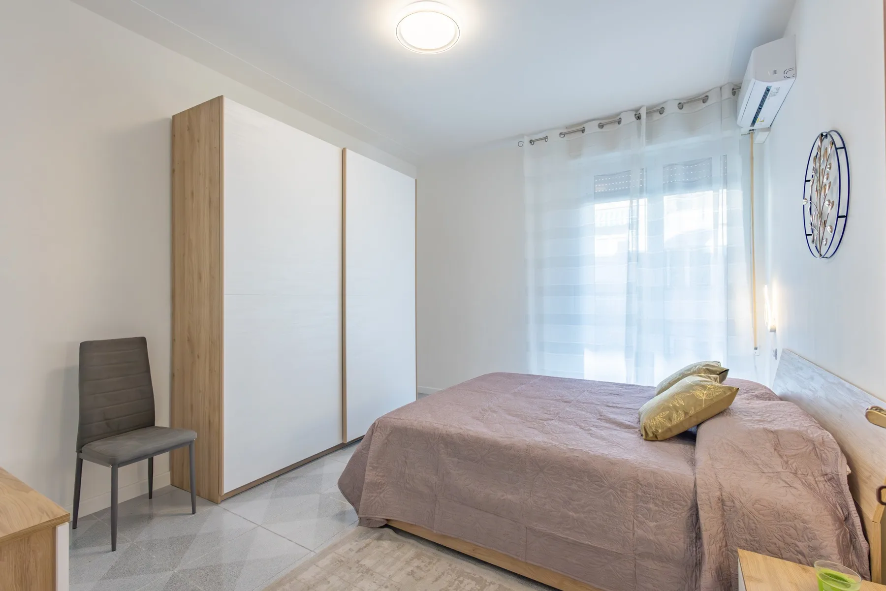 A bedroom with a bed, wardrobe, and a window covered by sheer curtains.