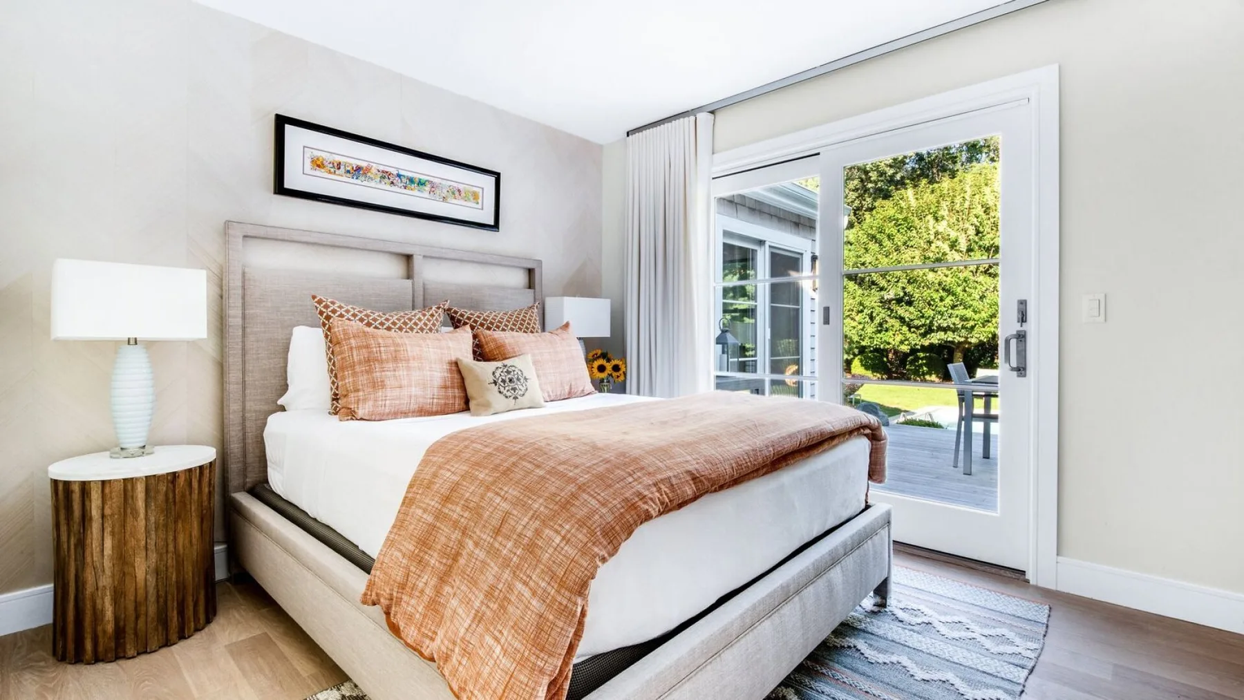 Un dormitorio con una cama vestida de blanco y tonos melocotón junto a puertas de vidrio.