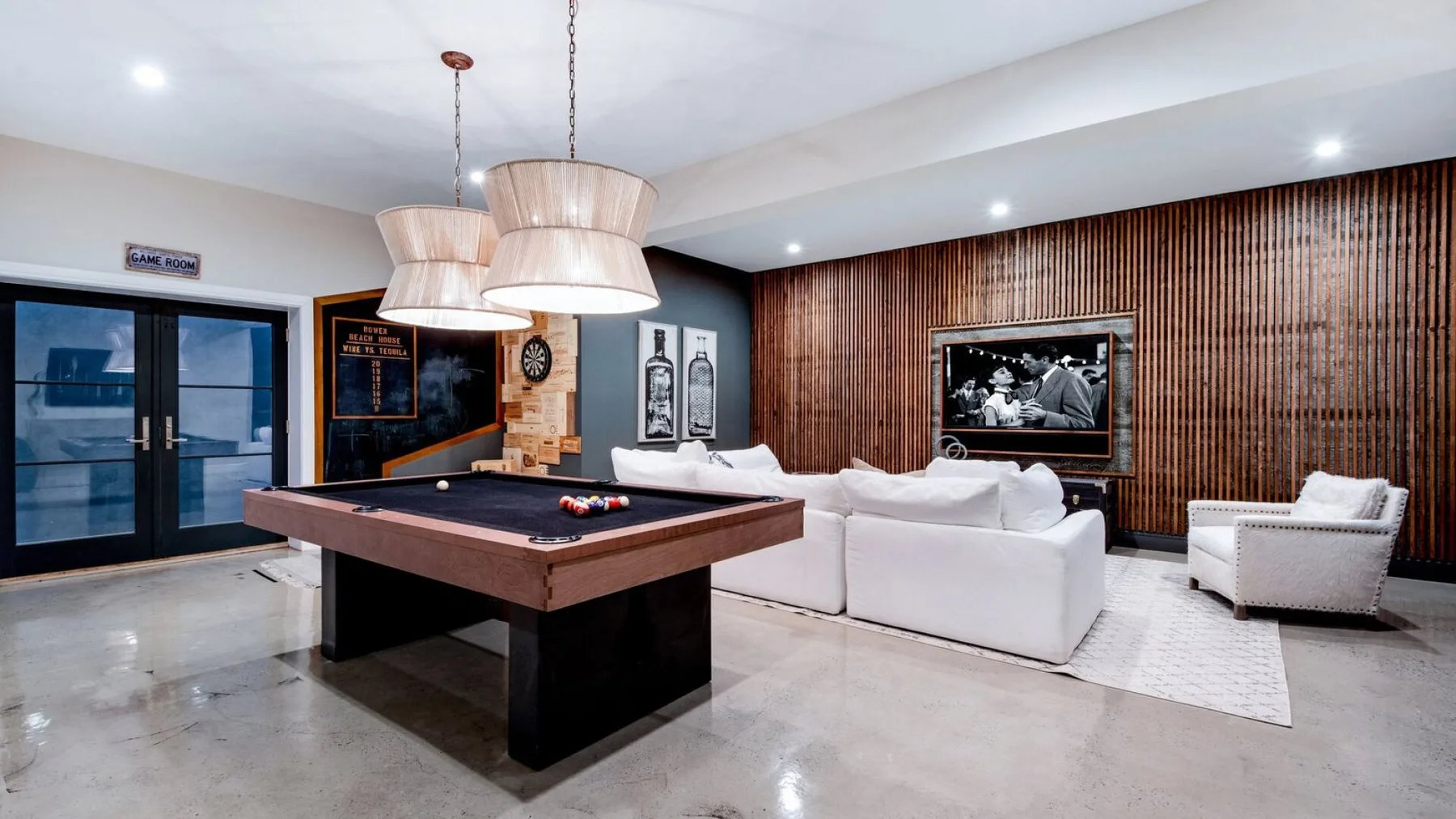 Una sala de estar con mesa de billar, asientos blancos y una pared de listones de madera.