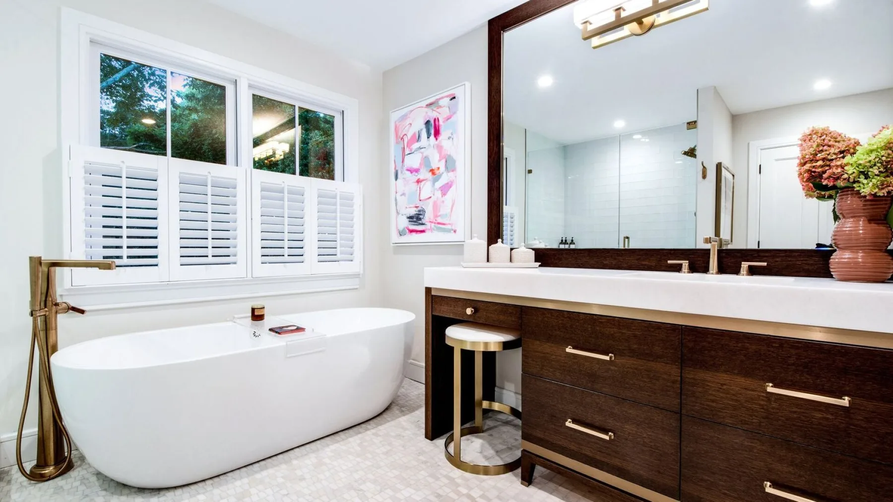 Un baño luminoso con una bañera exenta junto a un tocador de madera oscura.