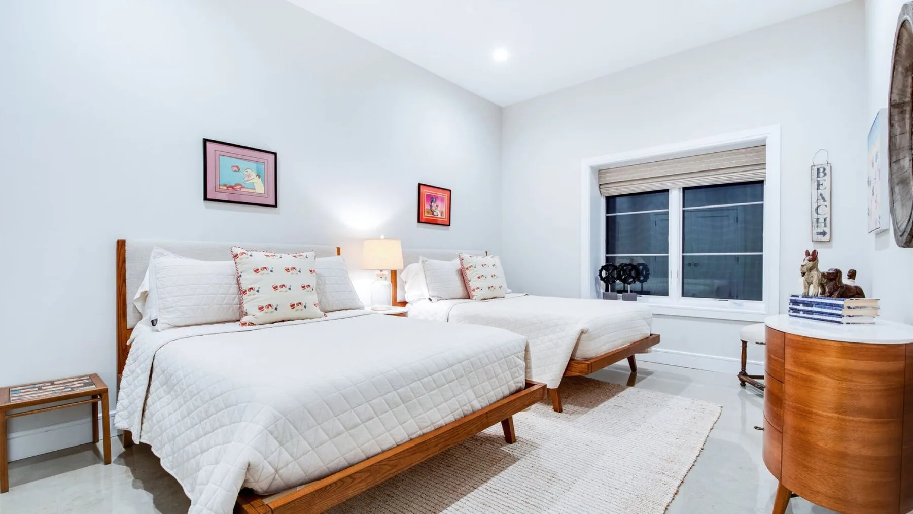 Un dormitorio luminoso con dos camas, una ventana y una cómoda de madera.