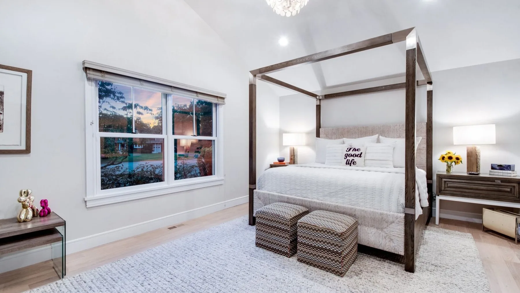 Un dormitorio luminoso con una cama con dosel y dos otomanas estampadas.