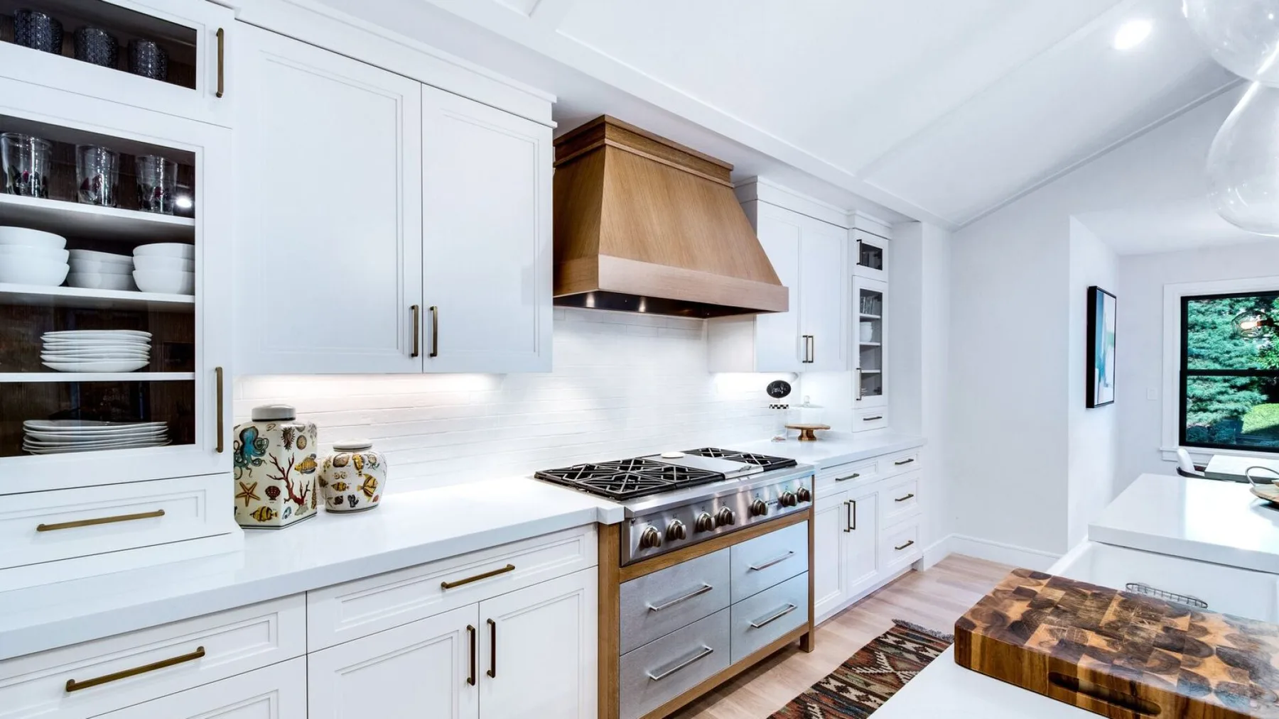 Una cocina blanca y luminosa tiene una estufa bajo una campana de madera.