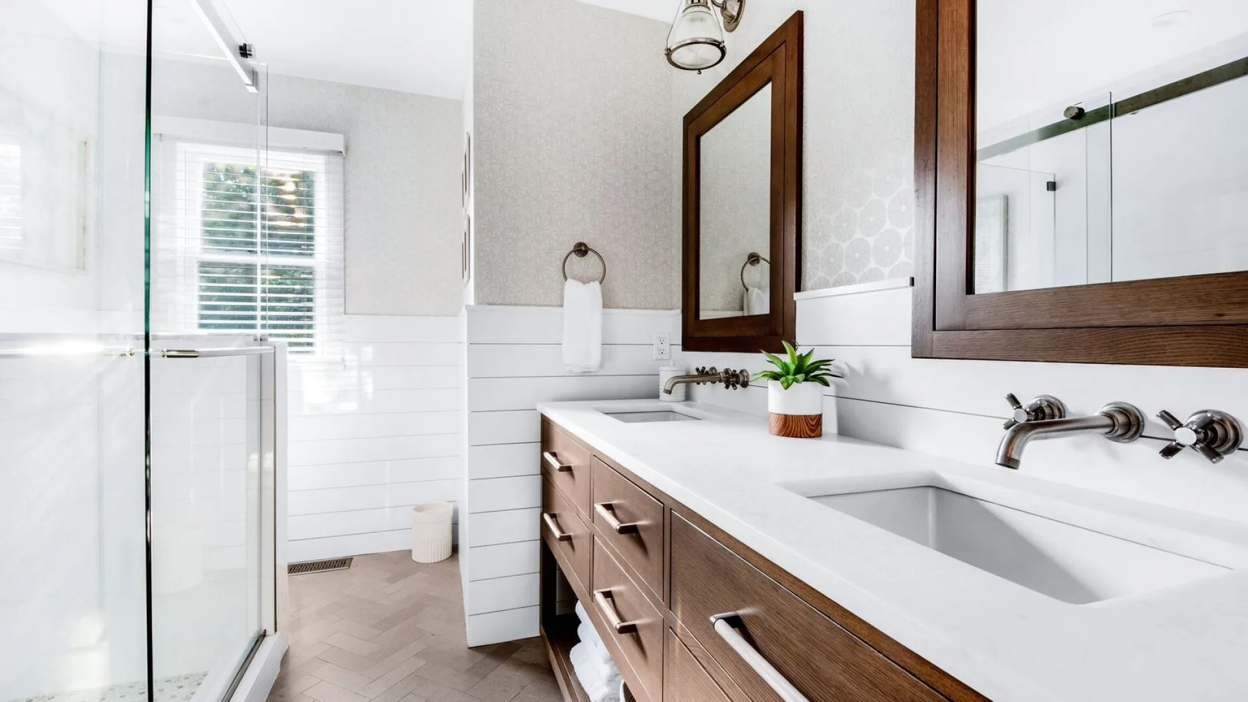 Un baño luminoso con lavabo doble, espejos y una ducha de vidrio.