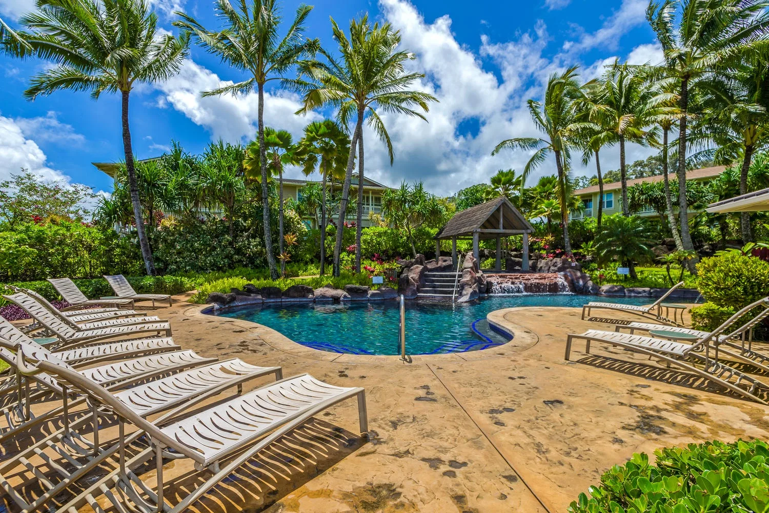 A tropical pool area with lounge chairs, palm trees, and a small gazebo.