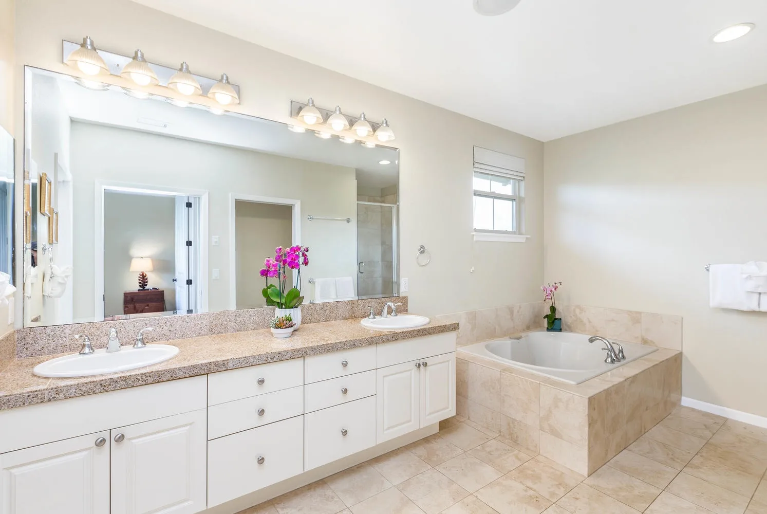 A bright bathroom with a long vanity, large mirror, and built-in soaking tub.