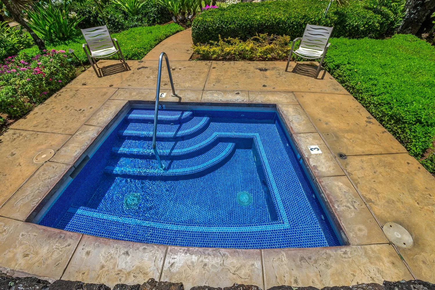 A small blue-tiled pool with curved steps sits in a paved garden area.