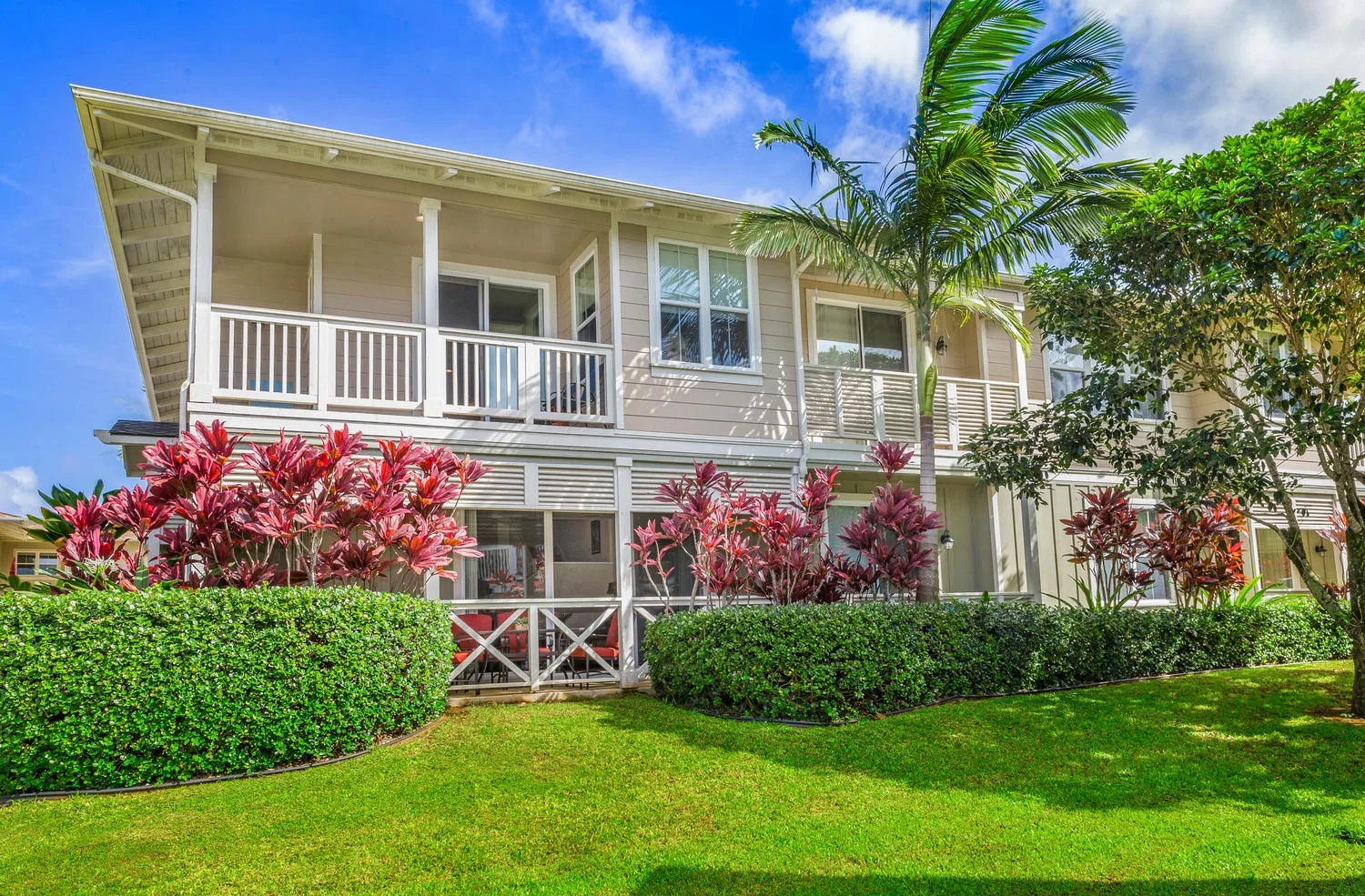 A two-story house with a covered balcony, palm trees, and landscaped lawn.