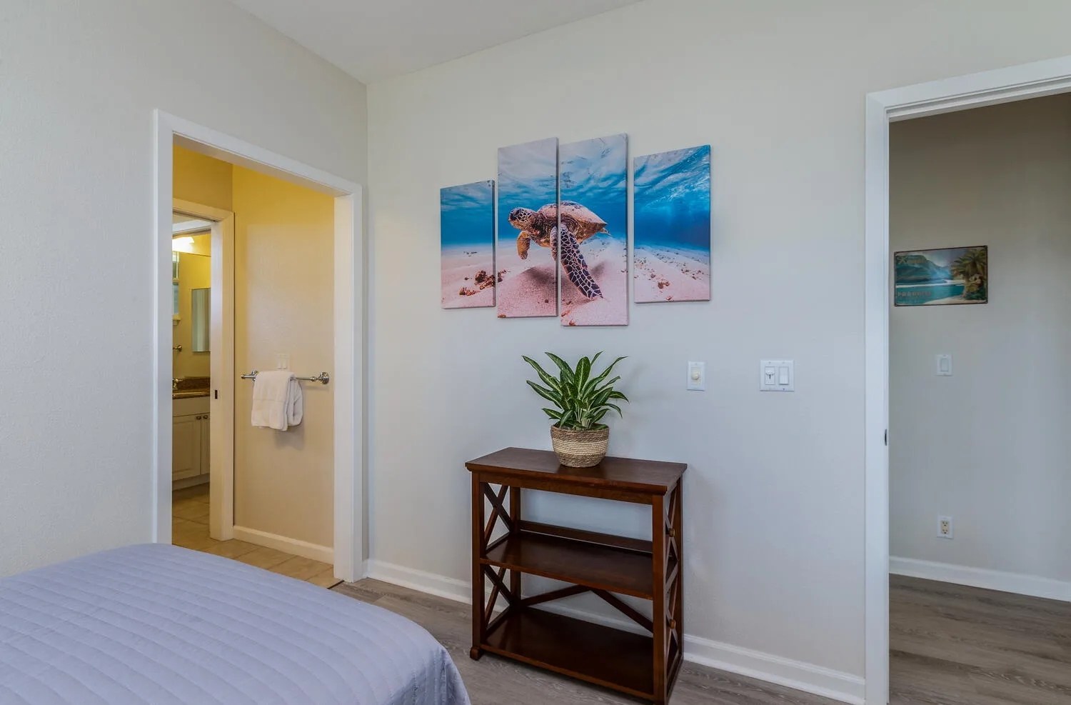 A bedroom with a wooden console table, a potted plant, and ocean-themed wall art.