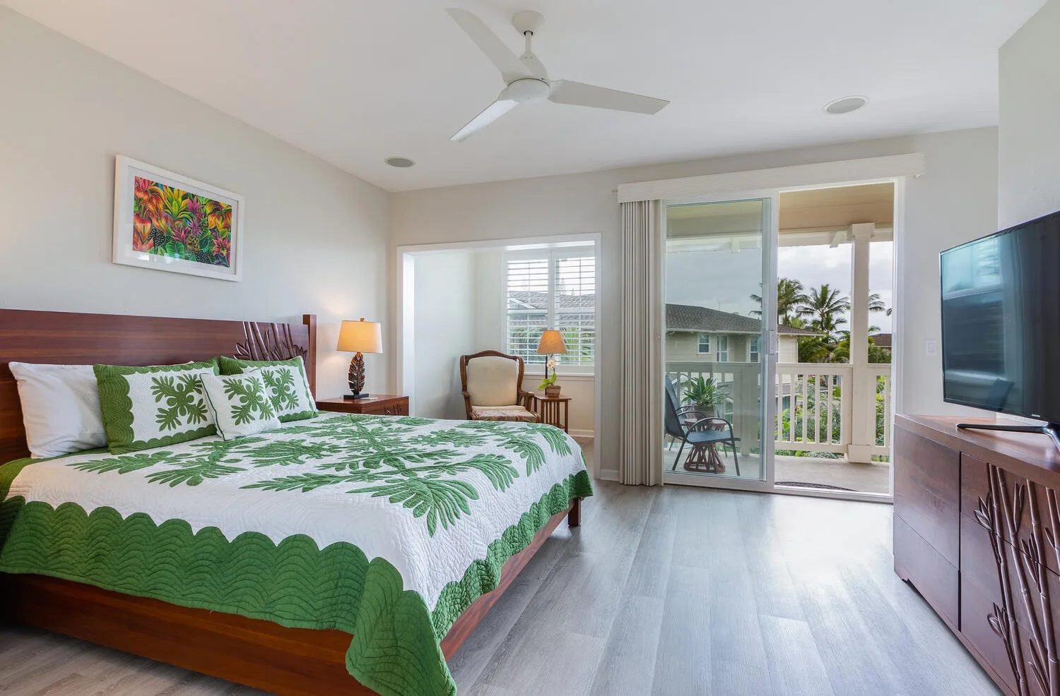 A bedroom with a leafy-patterned bedspread and sliding glass doors opening onto a balcony.