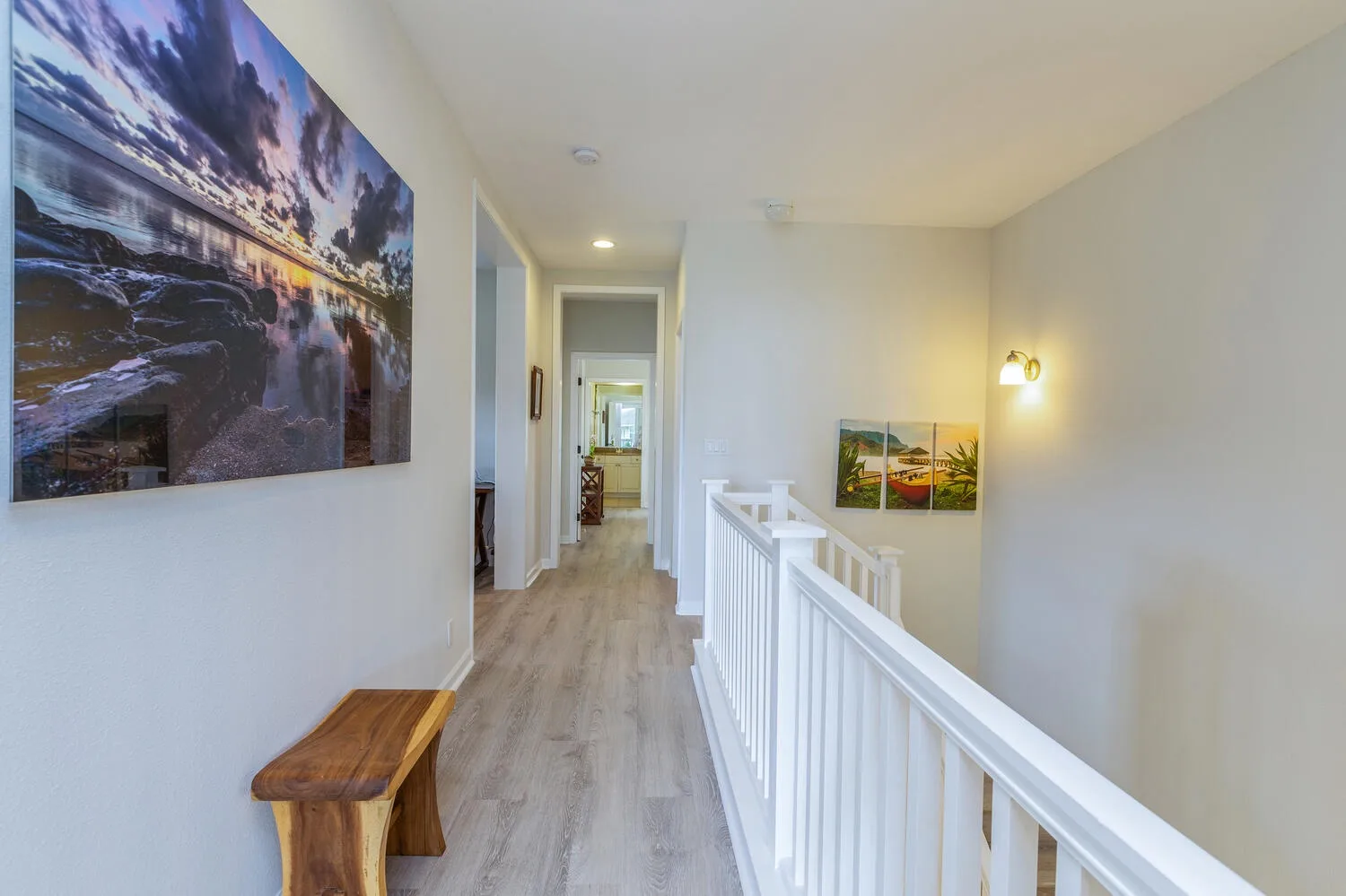 An upstairs hallway with light flooring, wall art, and a white railing.