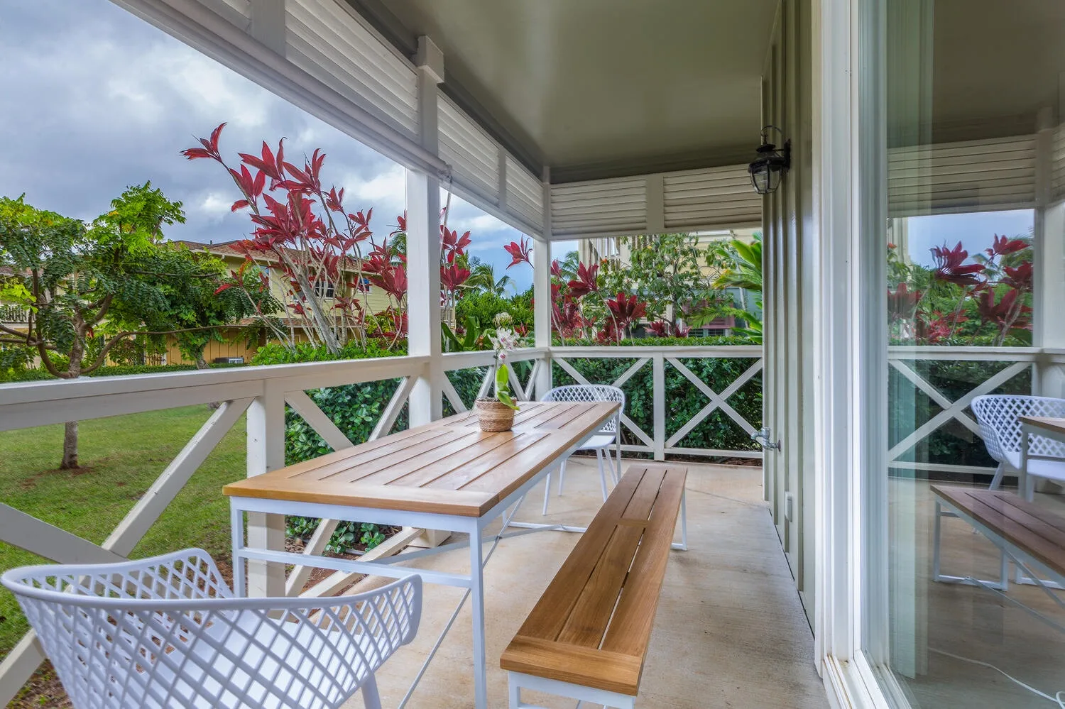 A covered patio has a long wooden table and bench beside garden views.