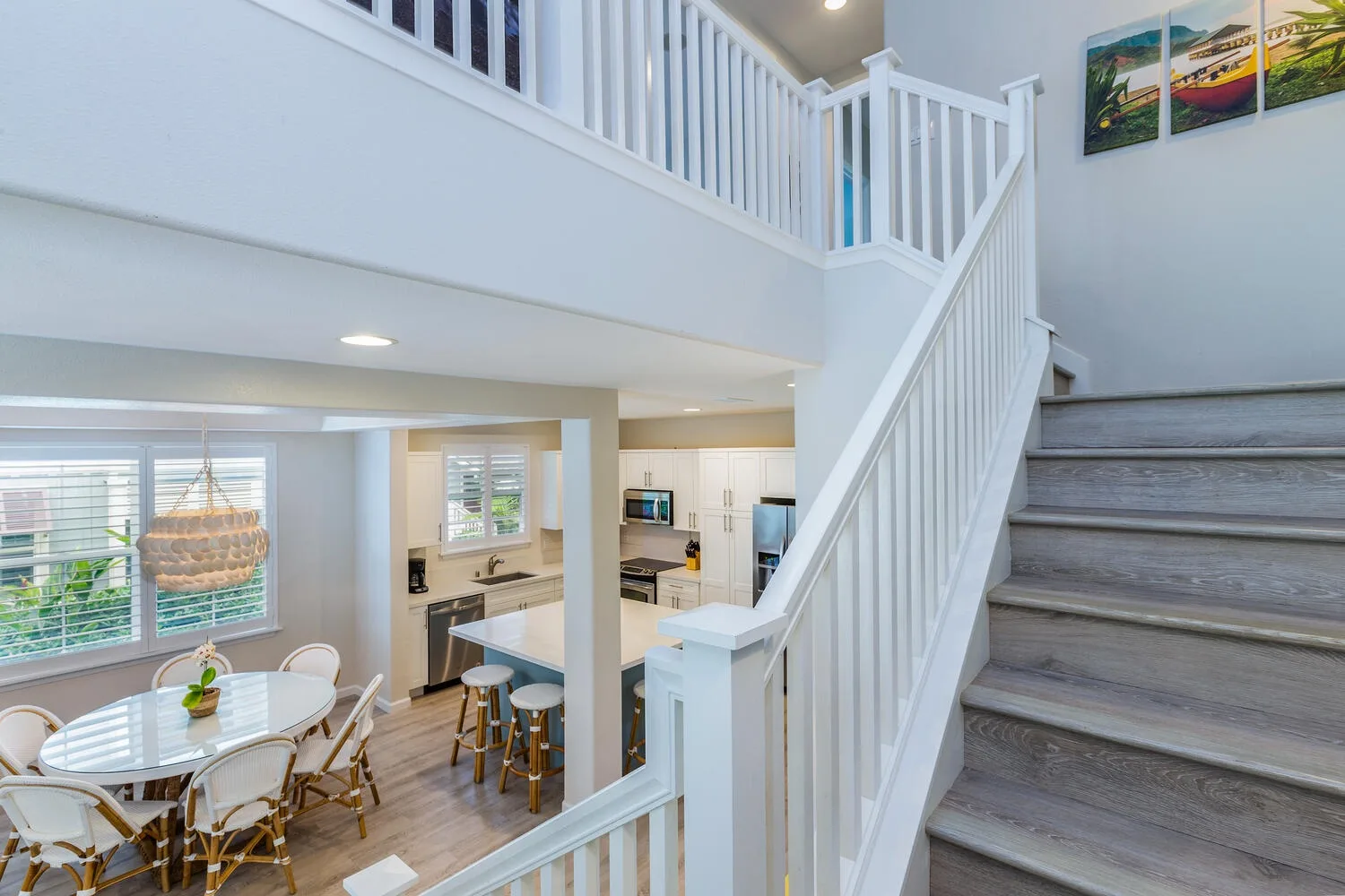 A bright open-plan living area with a kitchen beneath an upstairs landing and staircase.