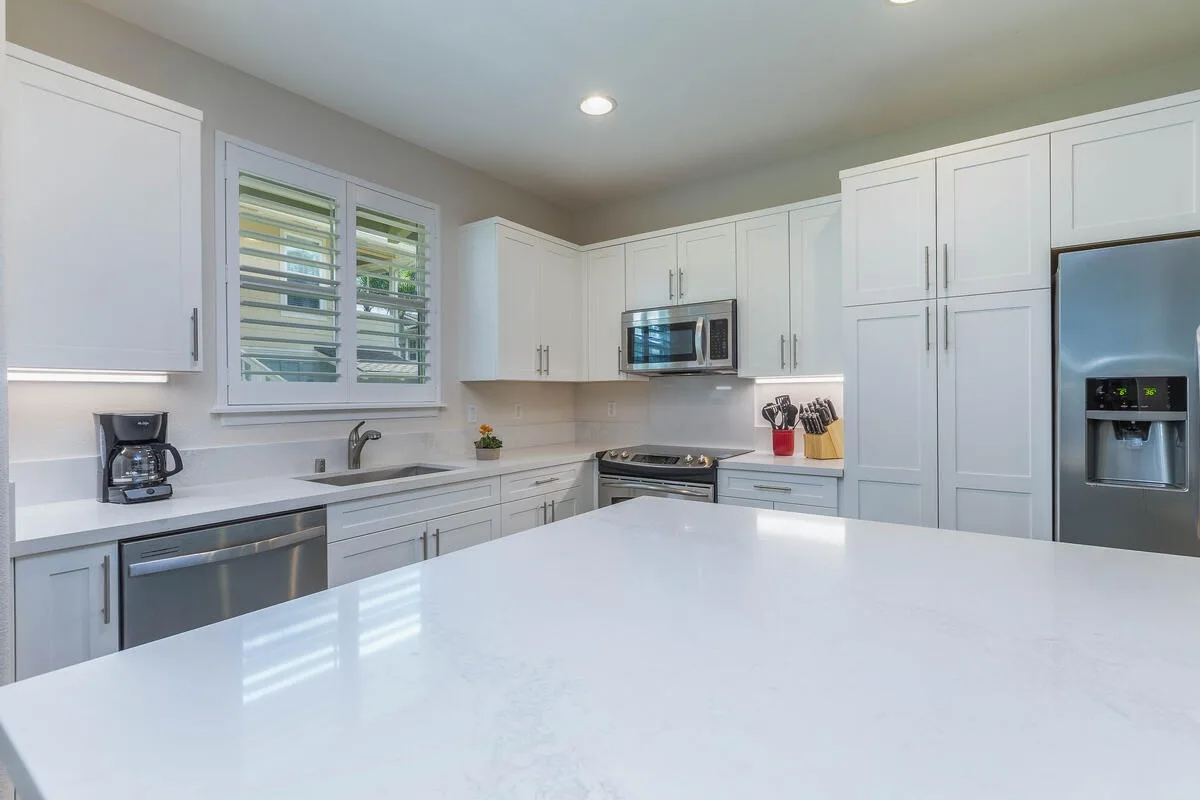 A bright kitchen with white cabinetry, a broad island, and stainless steel appliances.