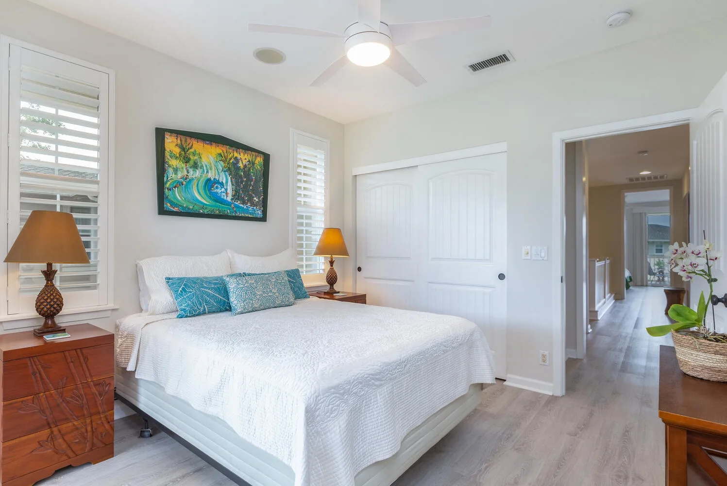 A bright bedroom with a neatly made bed and colorful artwork above it.