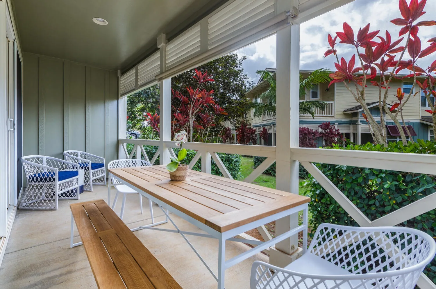 A covered outdoor seating area with a wooden table and benches overlooks greenery.