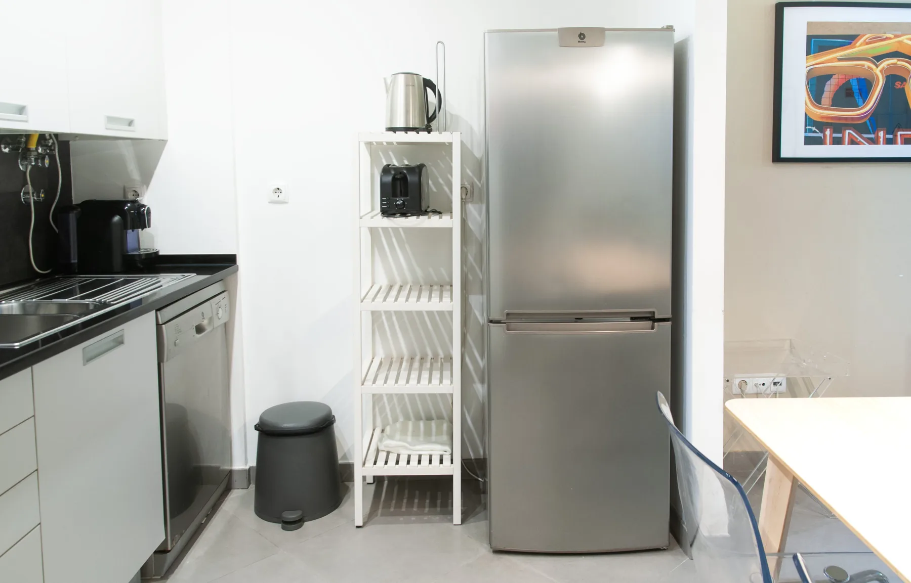 A compact kitchen with a stainless steel refrigerator and open shelving.